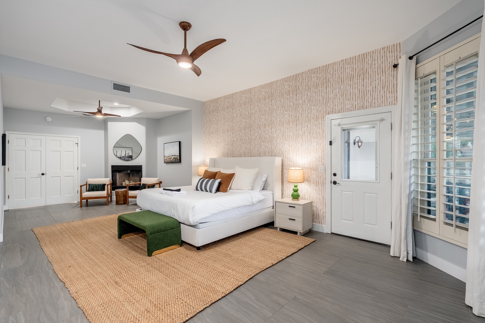 Your spacious bedroom sanctuary features a plush bed with layered linens, a cozy fireplace for cool evenings, and a private door to your own outdoor escape, all bathed in natural light.
