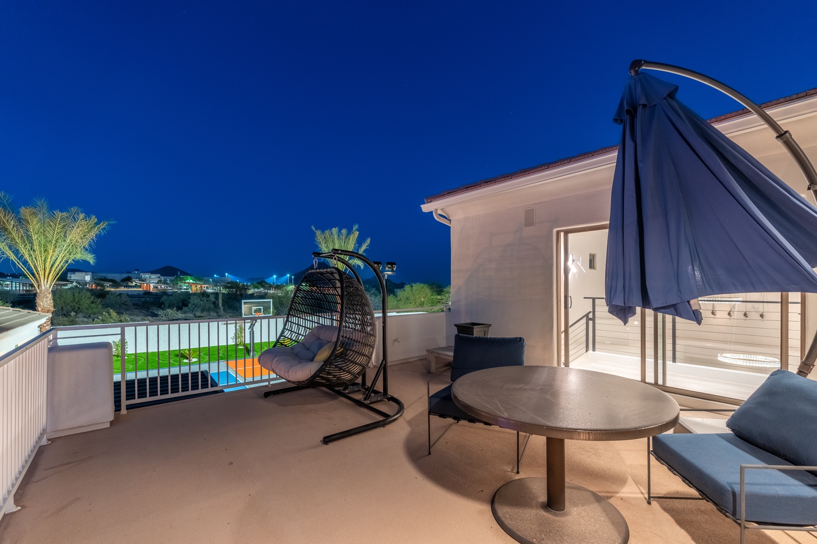 Unwind on your private terrace with a cozy swing seat, stylish outdoor seating, and a stunning night view of the sports court and palm-lined surroundings—your perfect evening escape.
