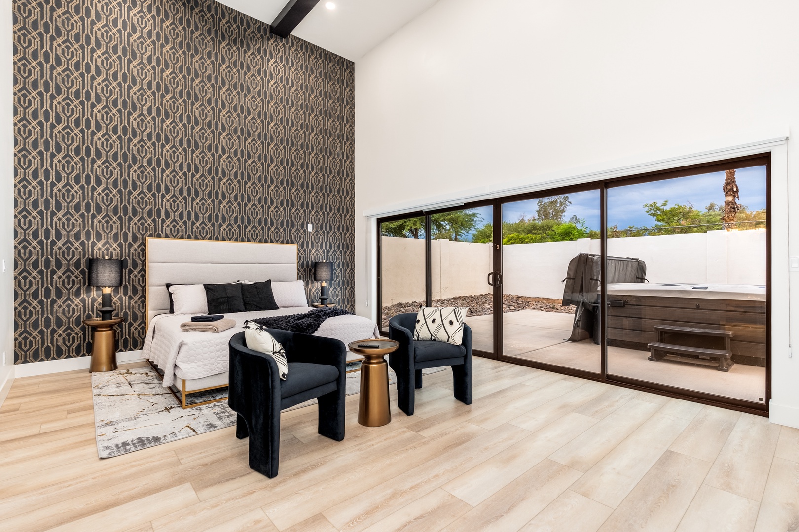 Your modern bedroom opens to a private patio with a hot tub, blending relaxation indoors and out under vaulted ceilings.