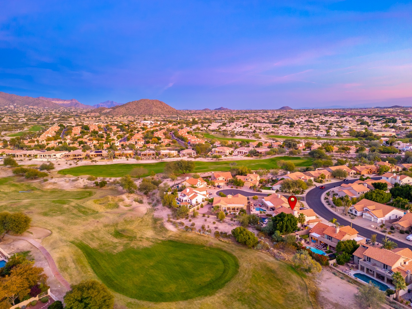 Aerial view of the property's location in a scenic desert golf community, surrounded by mountain views and neighboring amenities at sunset.