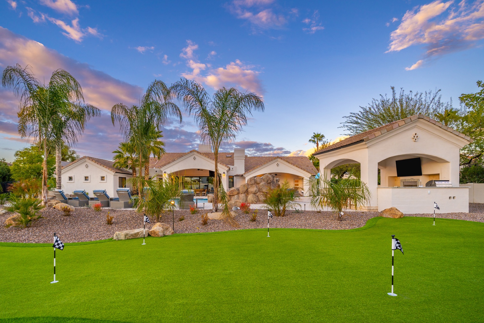 Stunning Spanish-style villa with palm-lined backyard putting green and outdoor entertaining areas set against vibrant sunset skies.