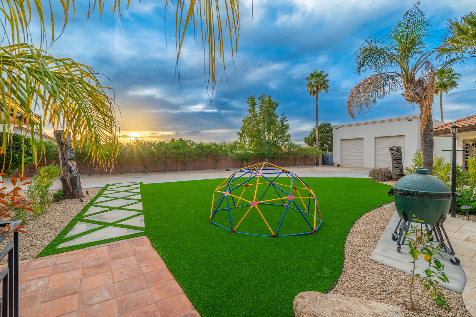 A spacious backyard features vibrant artificial turf, a colorful play dome, and mature palm trees framing peaceful views—ideal for outdoor fun and relaxation.