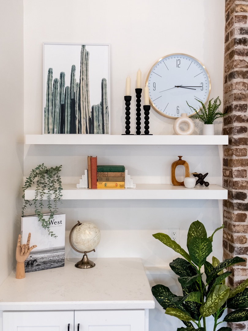 Stylish shelving with curated décor—cactus art, plants, books, and a wall clock—creates a cozy corner where you can settle in and feel right at home.