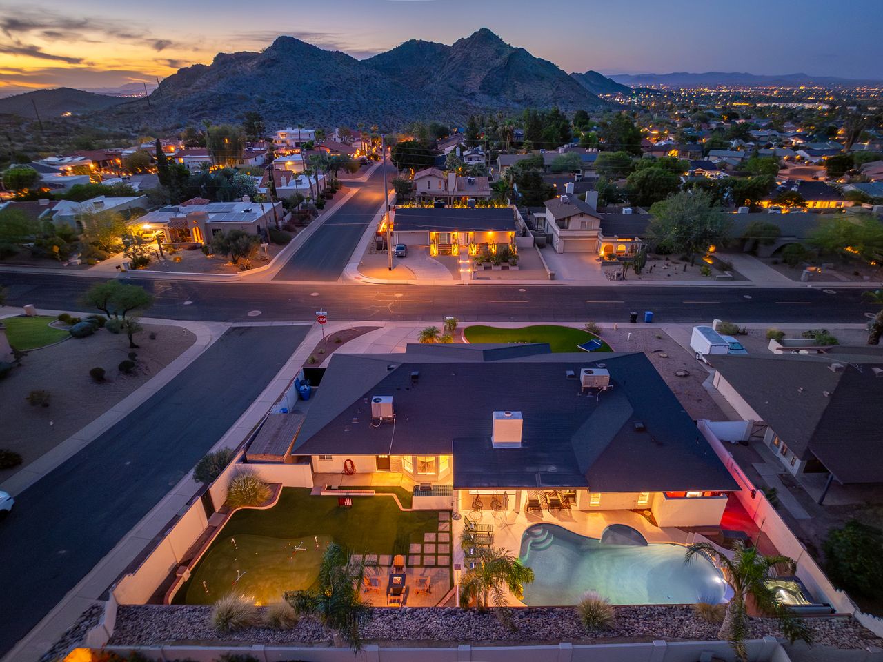 Stunning aerial view of a modern desert retreat nestled in a scenic neighborhood with dramatic mountain backdrop and city lights at twilight.