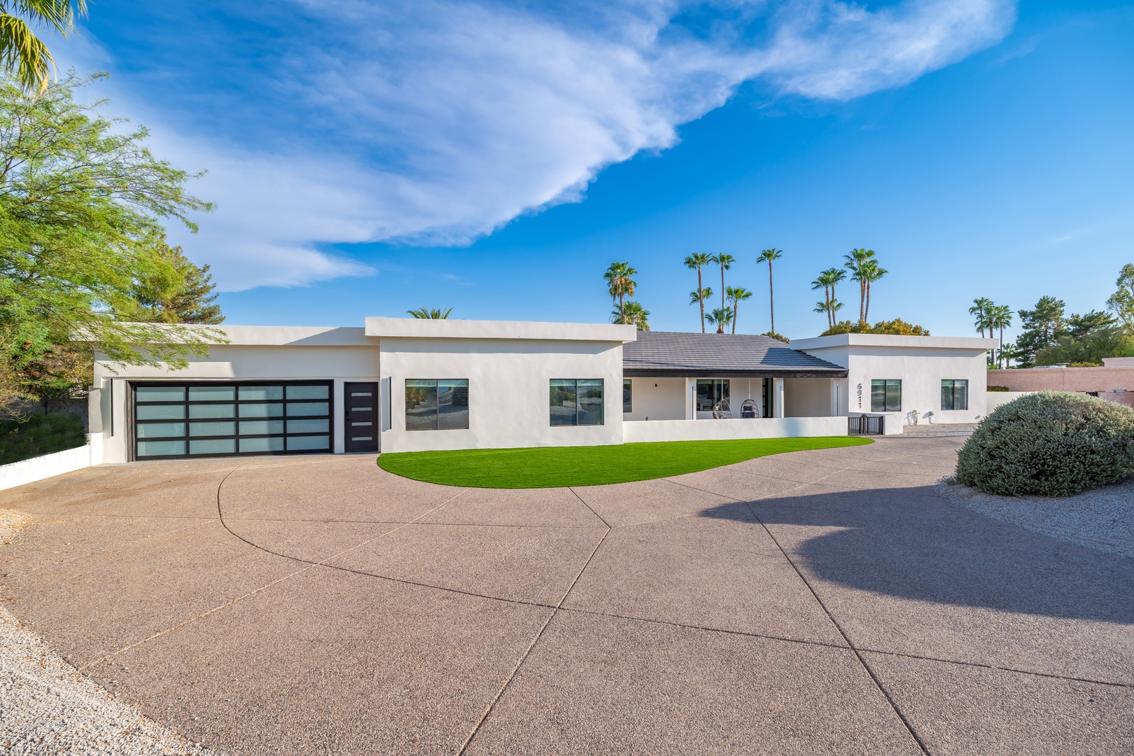 A striking modern desert retreat with clean lines and contemporary architecture, framed by swaying palms and lush landscaping under Arizona skies.