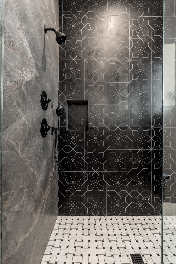 Your luxurious rain shower awaits behind elegant glass, featuring striking geometric tiles and matte black fixtures that blend sophistication with comfort—perfect for unwinding after a day of exploring.