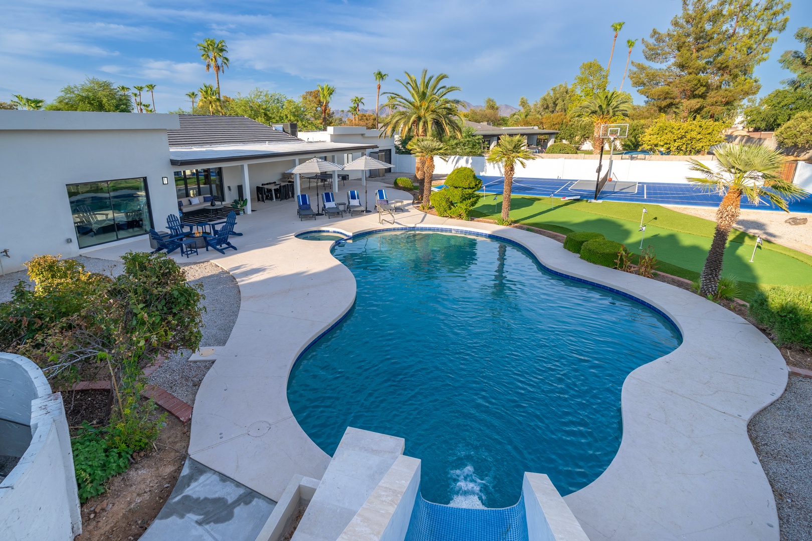 This aerial view showcases the expansive property grounds, featuring a sparkling pool and lush landscaping surrounded by palm trees and recreational areas including a tennis court and putting green.