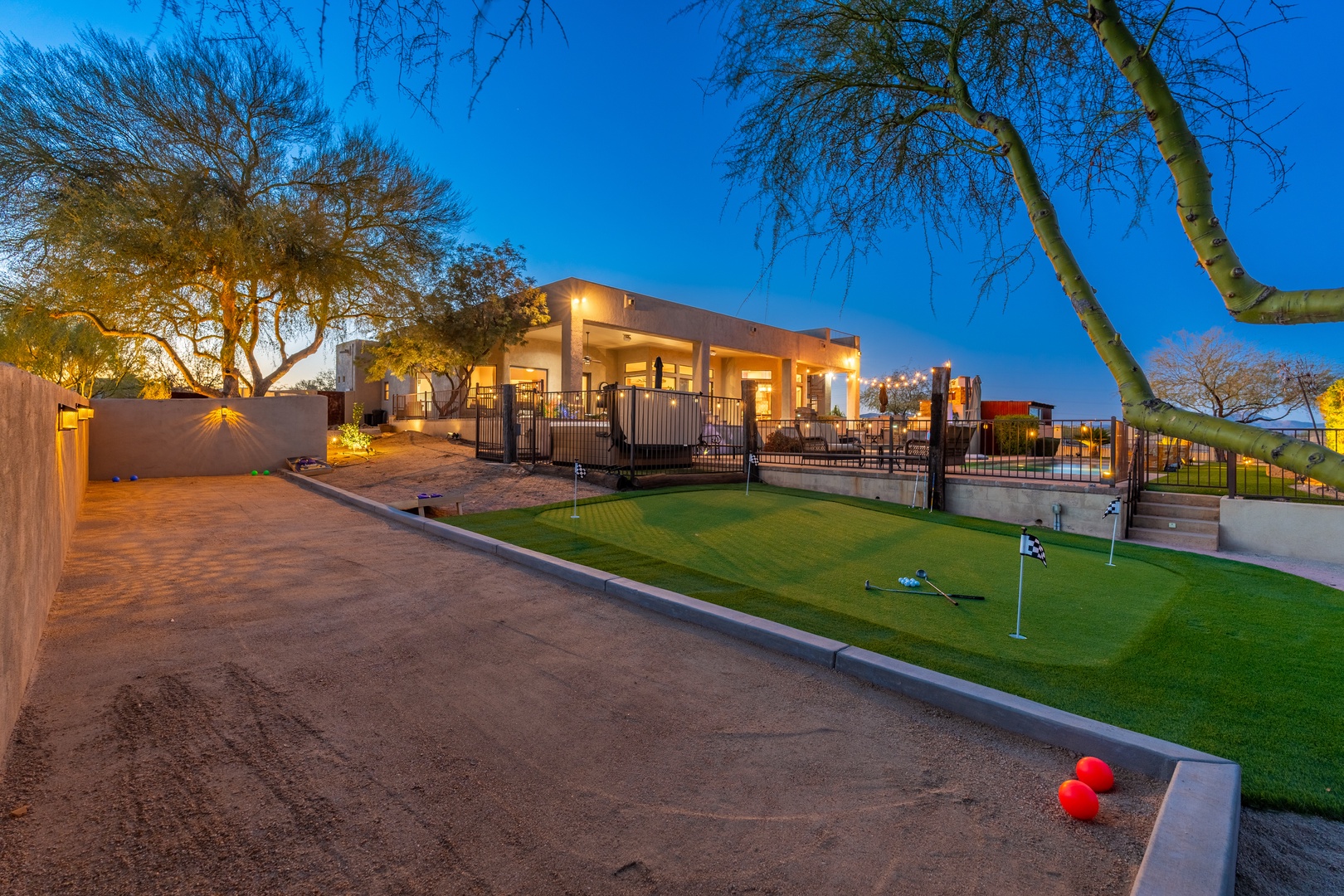 Twilight illuminates the property's expansive outdoor recreation area, complete with putting green and bocce court, all set beneath a brilliant desert sky framed by mature trees.