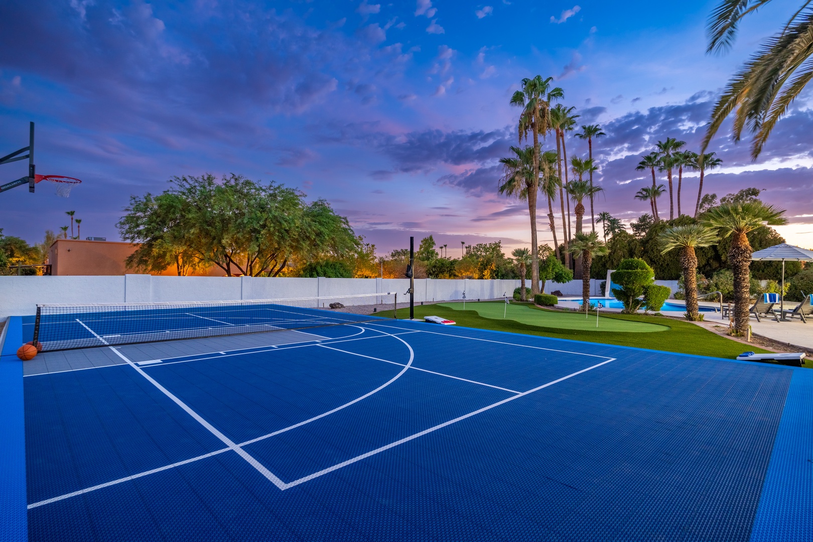 A private multi-sport court awaits beneath a stunning desert sunset, framed by palms and backing onto a sparkling pool and lawn—ready for your friendly matches or pick-up games.