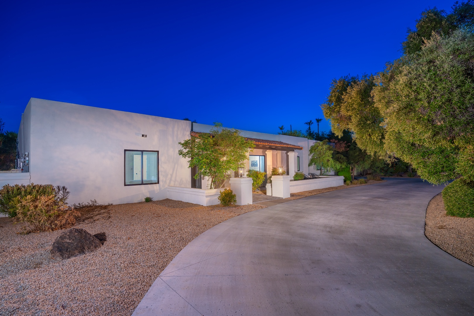Modern desert retreat with striking white adobe architecture, framed by lush landscaping and sweeping blue skies. Your private drive leads to a serene sanctuary where contemporary design meets natural beauty.