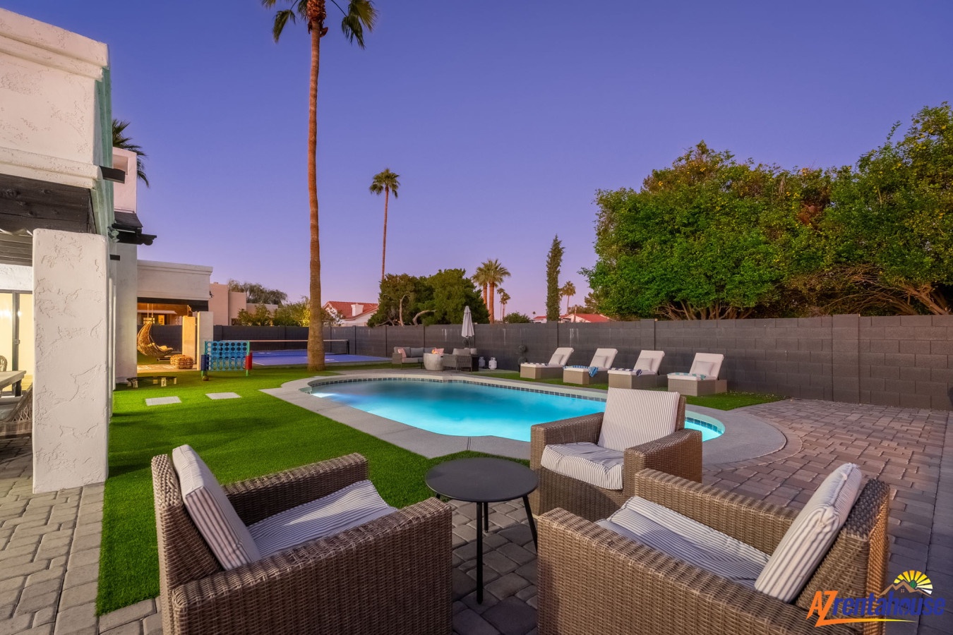 Modern backyard oasis with sparkling pool, comfortable seating, and palm trees under desert twilight skies.