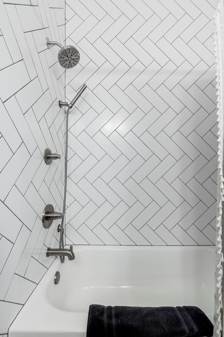 Sleek white herringbone tile wraps your private bath, complete with a modern shower-tub combo and handheld sprayer for your comfort.