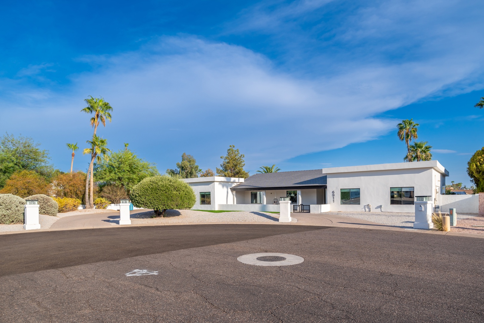 A modern, single-story vacation home set in a serene desert neighborhood, framed by palm trees and lush landscaping under bright Arizona skies.