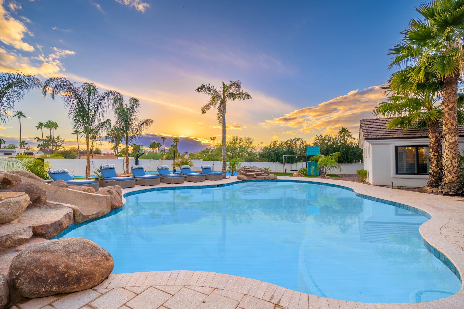 This resort-style pool with natural rock features and tropical palms creates the perfect desert oasis for your vacation, framed by stunning sunset skies.
