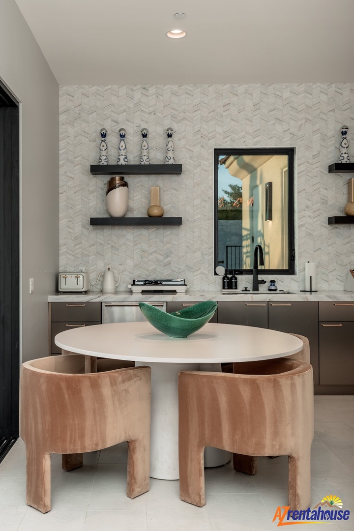 Your stylish dining nook features a sleek round table with curved wooden stools, perfect for intimate meals beneath elegant herringbone tiles.