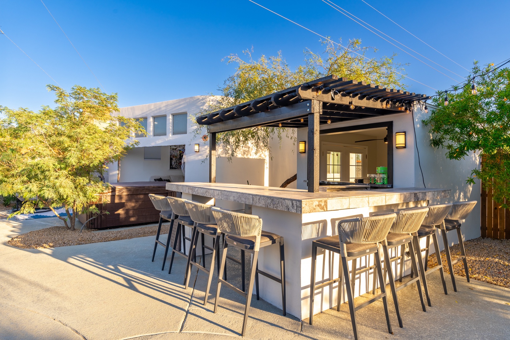 Modern outdoor bar with sleek seating invites relaxed evenings under the pergola, framed by lush greenery and warm lighting for effortless entertaining.