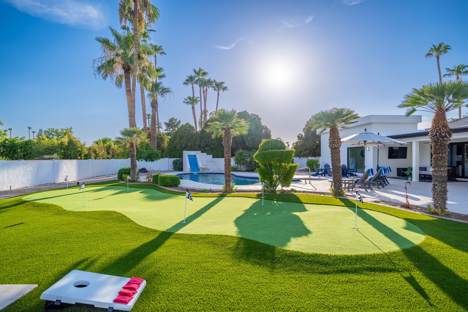Sunny desert oasis featuring a private backyard with miniature golf course, sparkling pool, tropical palms, and outdoor seating perfect for friendly competition and relaxation.