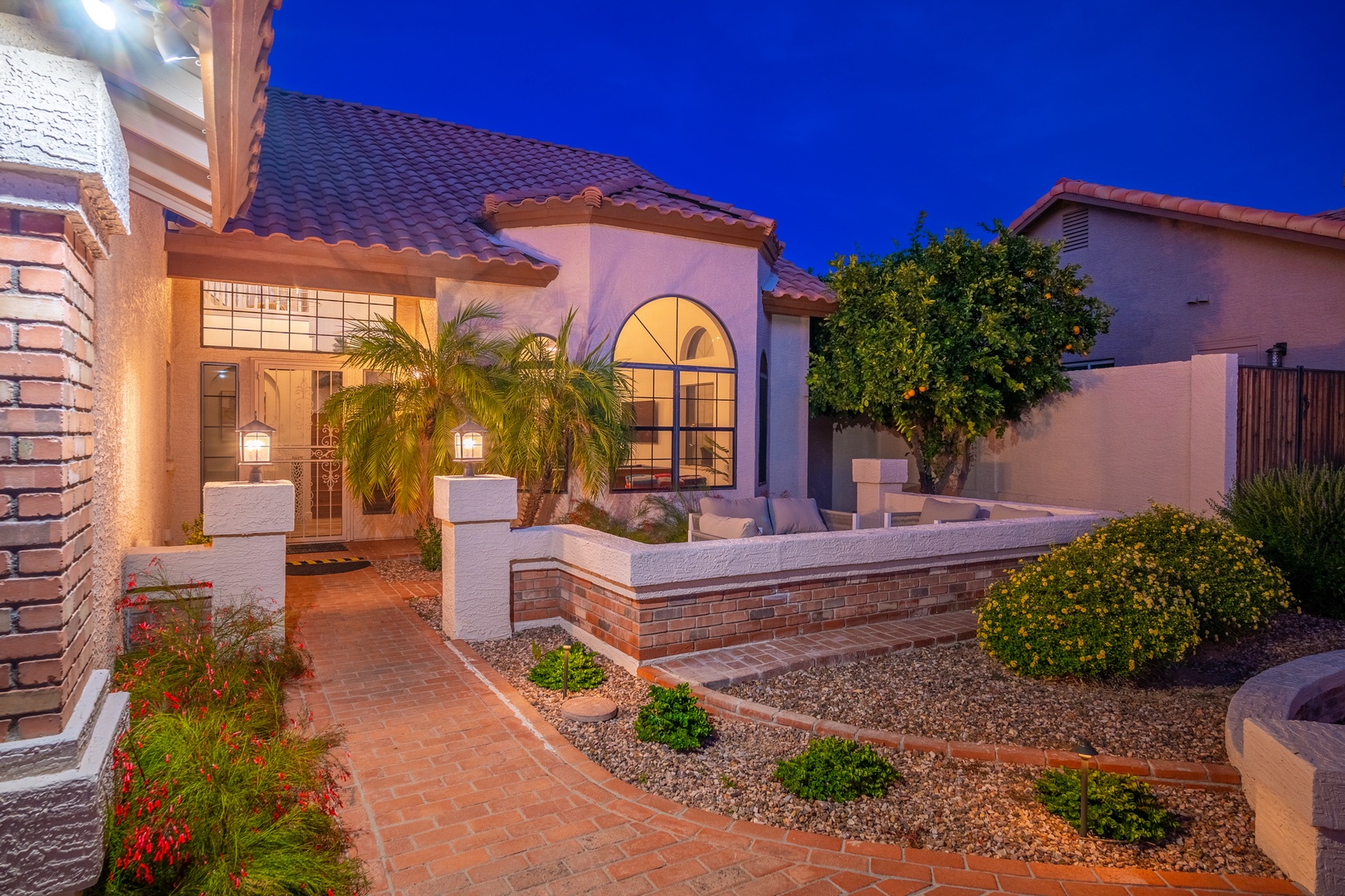 This inviting Spanish-style home features warm lighting and lush landscaping in a quiet residential neighborhood, welcoming guests at dusk with classic architectural charm.