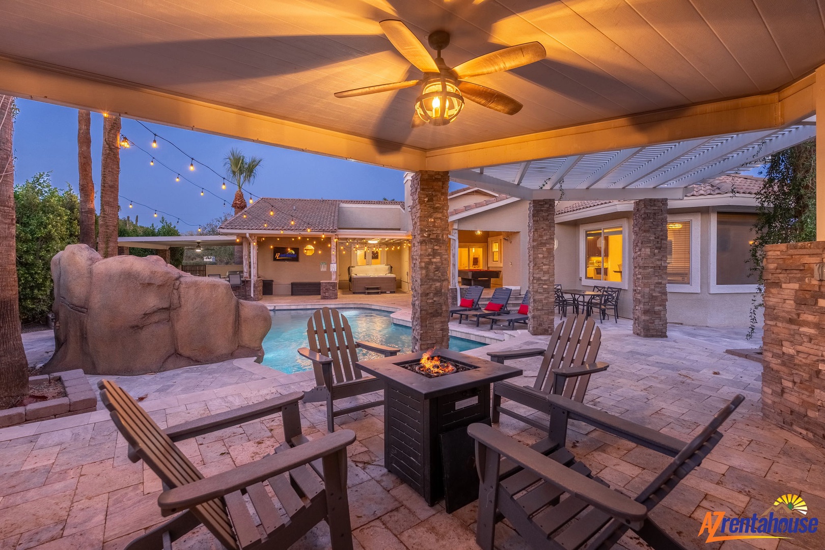 Your evening oasis awaits with a glowing fire pit, inviting pool with rock waterfall, and twinkling lights overhead. Gather here for unforgettable desert nights under covered comfort.