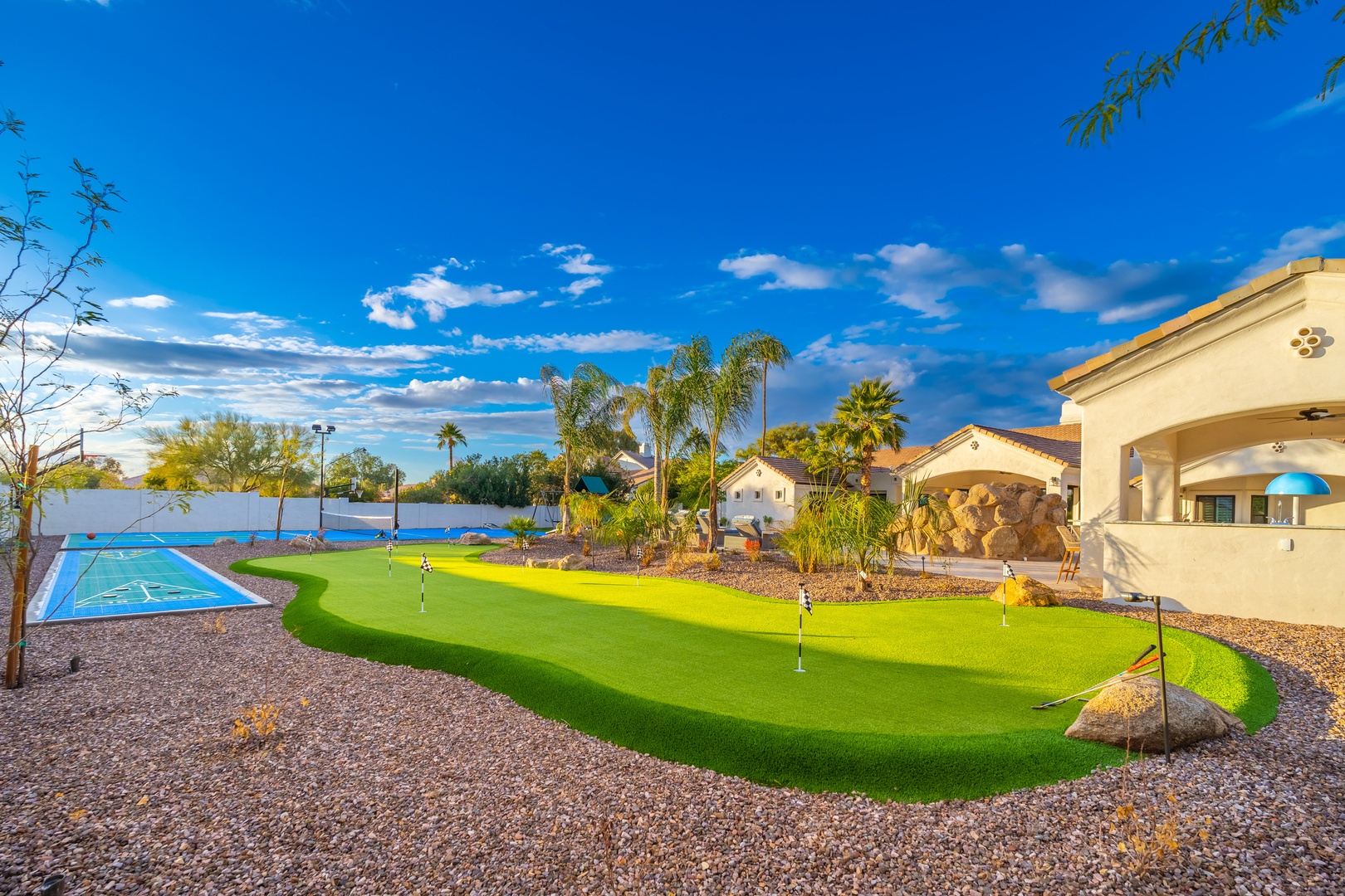 Private backyard oasis featuring a custom putting green, sport court, and lush landscaping under sunny Arizona skies. Perfect for outdoor recreation and entertaining.