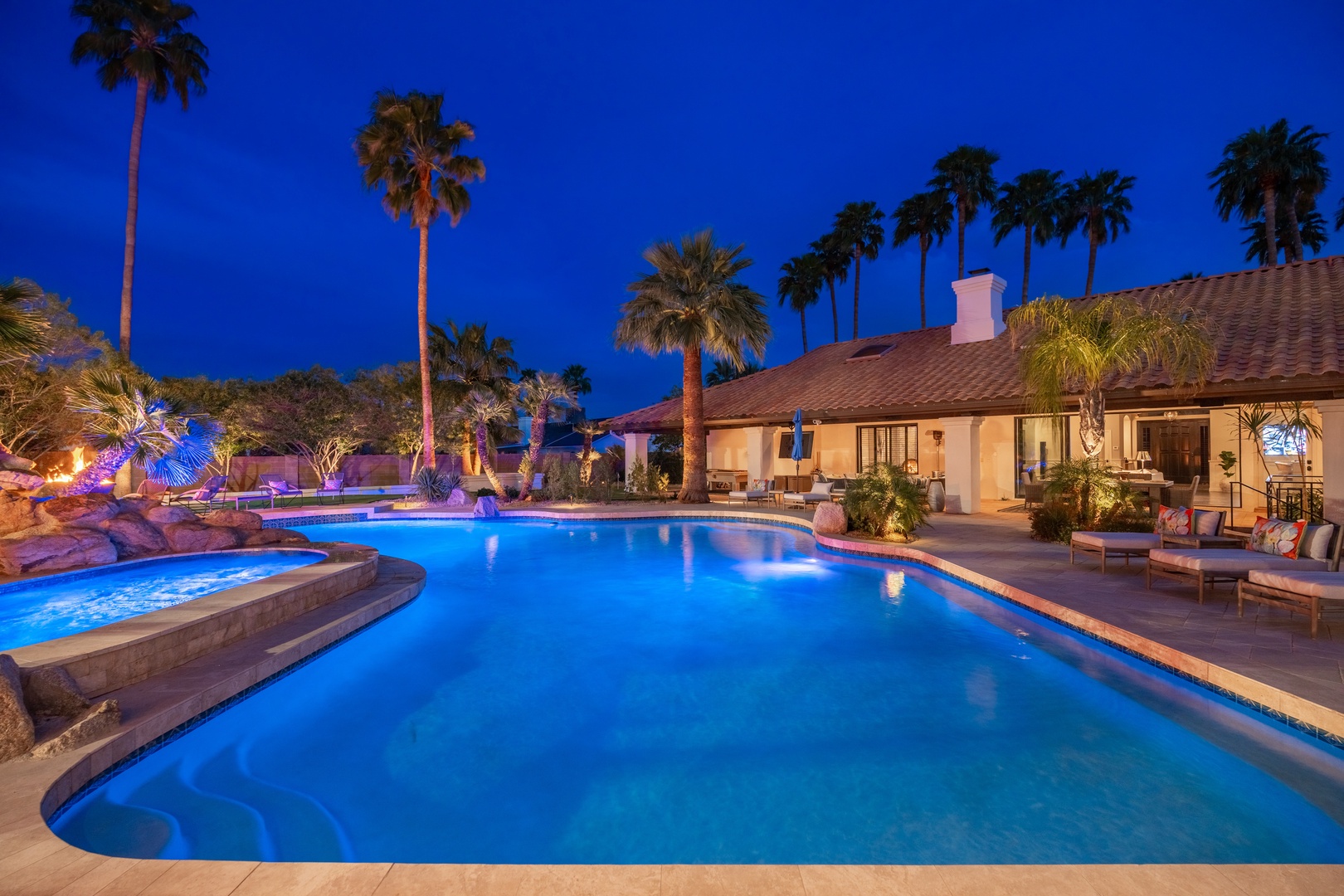 This private resort-style backyard features a sprawling pool, spa, and palm-lined oasis under dramatic twilight skies—perfect for luxurious desert evenings.
