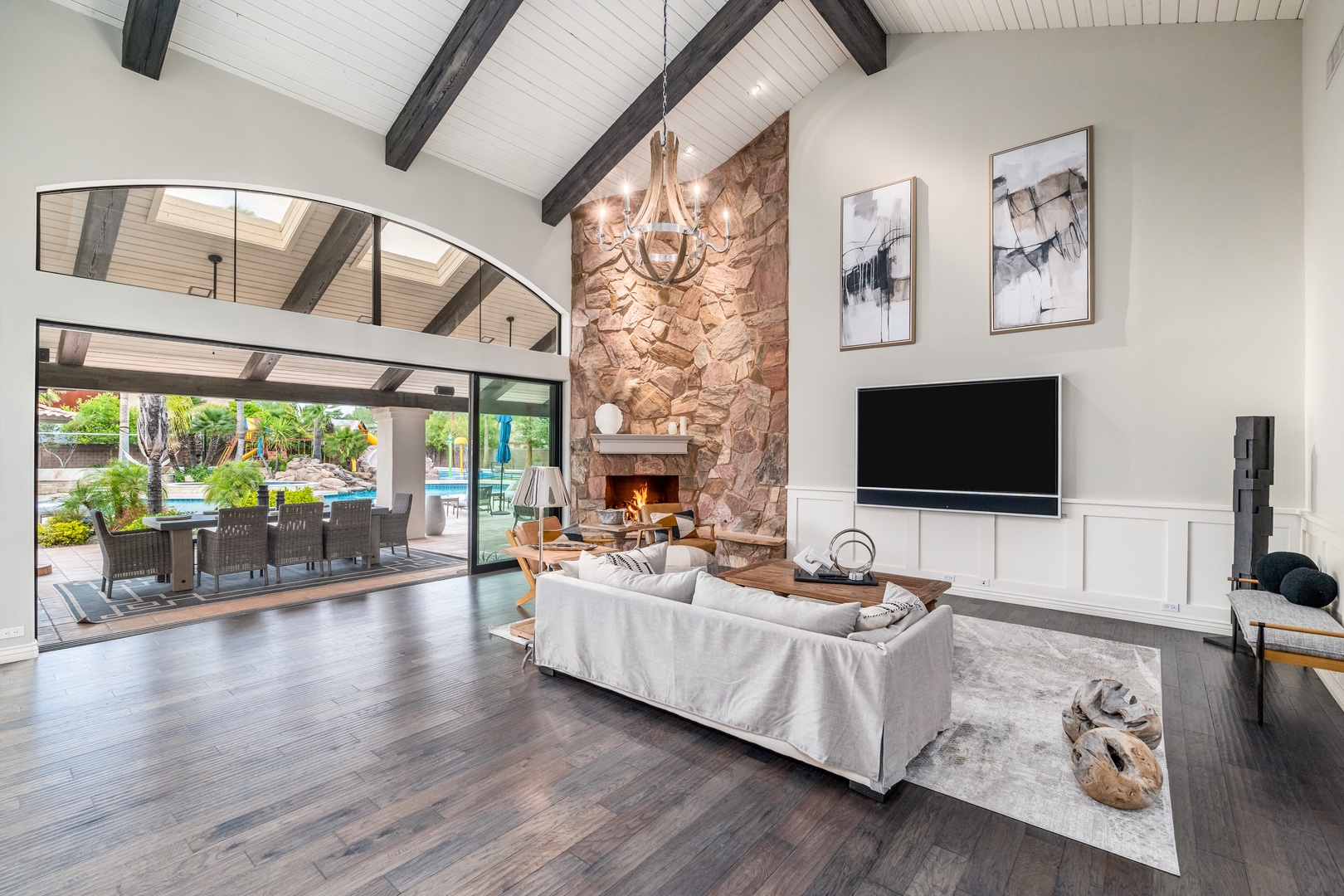 Settle into this stunning living space with soaring beamed ceilings, a grand stone fireplace, and floor-to-ceiling windows opening to your private pool and patio—perfect for gathering with loved ones.
