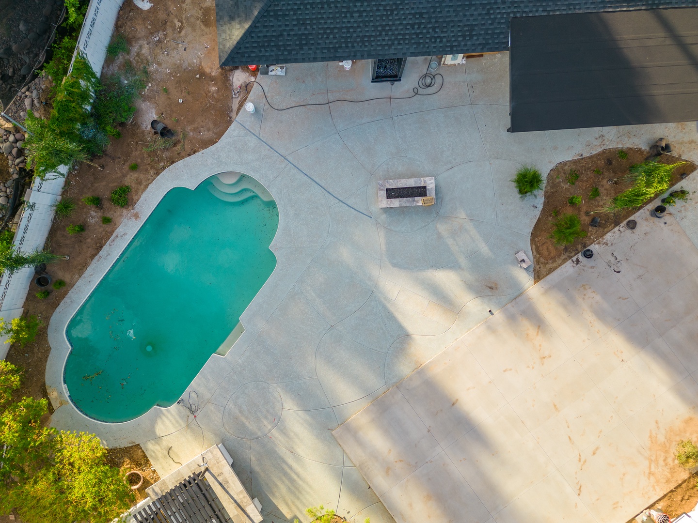 Aerial view of the property's pool and surrounding outdoor space, featuring a uniquely shaped swimming pool and a spacious patio area with garden landscaping.