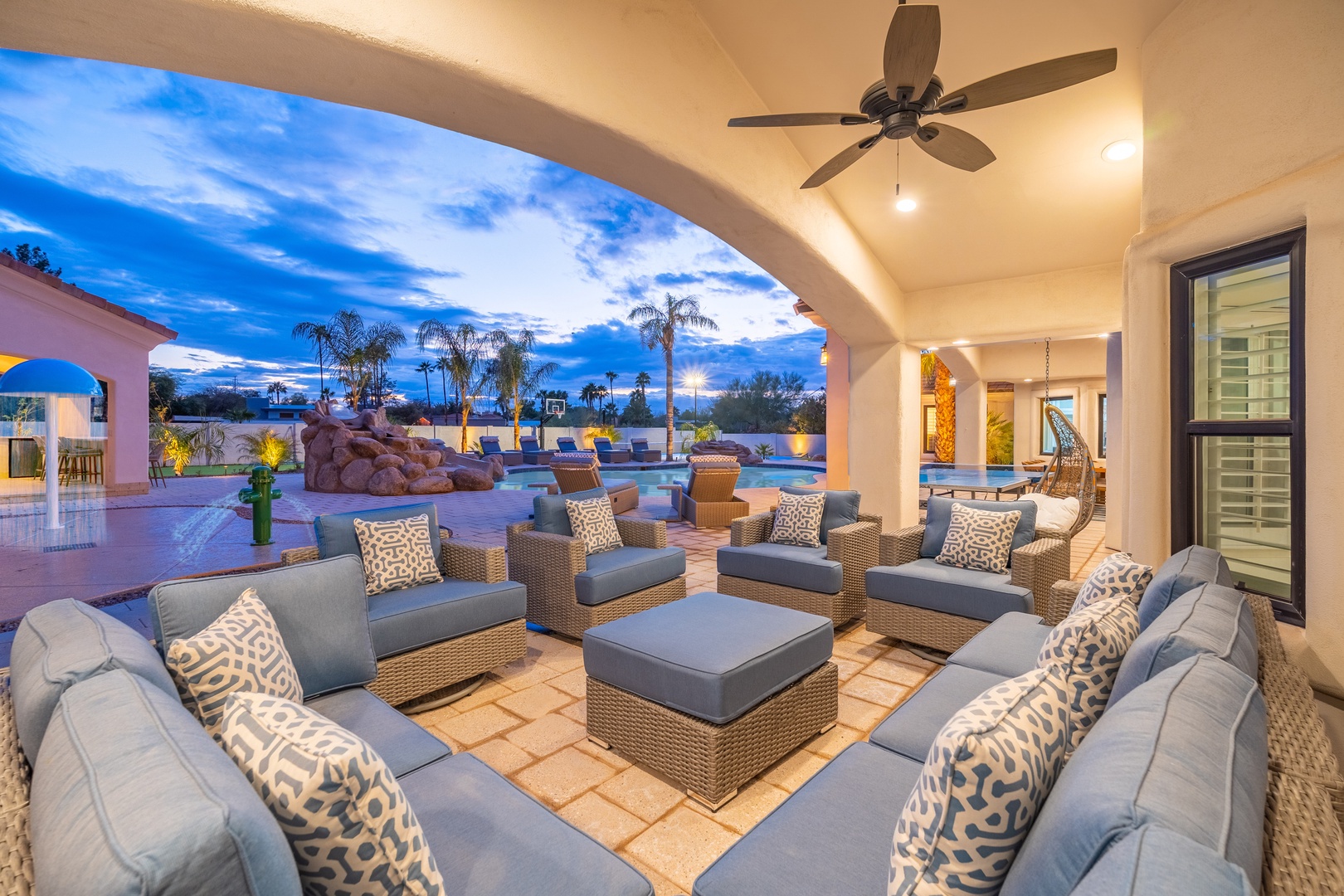Unwind in this stunning covered patio with plush seating perfect for evening gatherings. The space opens to a sparkling pool and lush desert palms, blending comfort and tropical elegance.