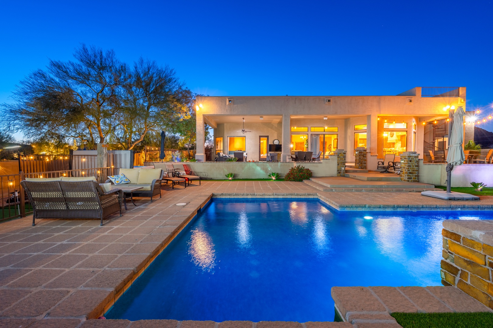 A sparkling pool glows at dusk, inviting you to unwind on comfortable loungers while the warm desert evening settles around this beautifully lit modern retreat.