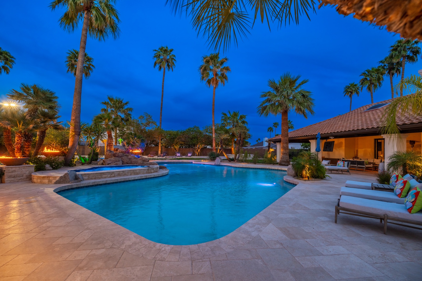 Your private oasis awaits—a stunning pool surrounded by swaying palms, warm evening lighting, and inviting loungers for ultimate relaxation under the stars.