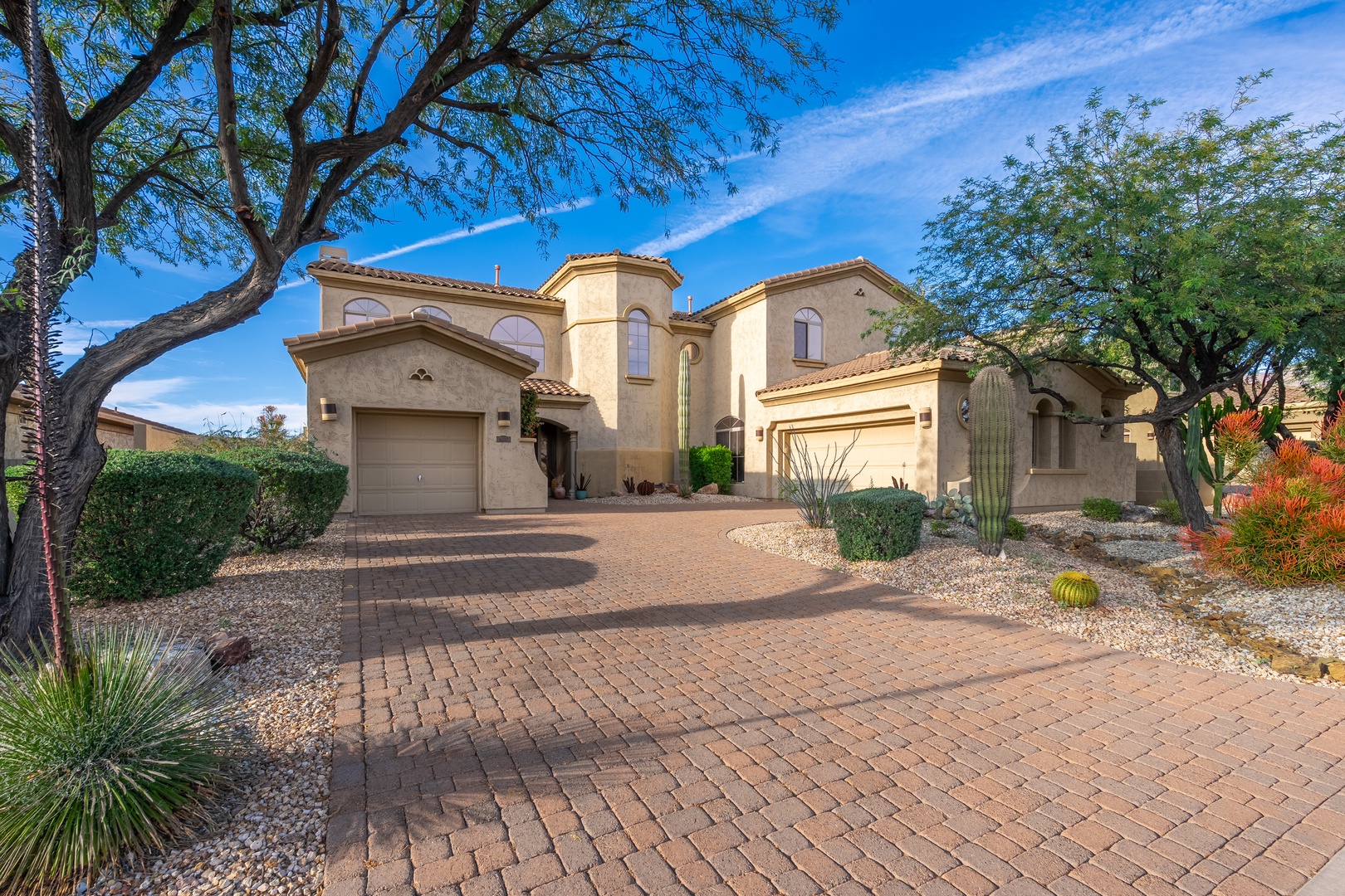Spacious desert-style property with elegant stucco architecture, mature desert landscaping, and ample parking on a peaceful residential street.