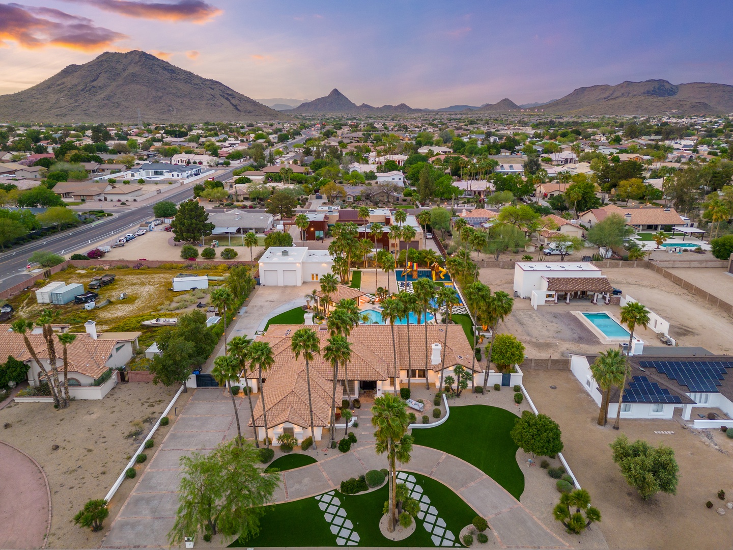 Aerial view of the property nestled in a scenic desert neighborhood, framed by dramatic mountain ranges and colorful skies at dusk.
