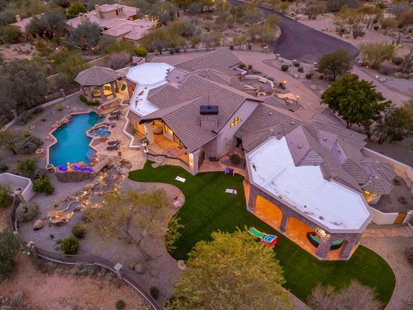 Expansive desert estate with private pool, lush lawns, and covered patios set within the natural Sonoran landscape. Nearby homes dot the hillside along quiet residential roads.