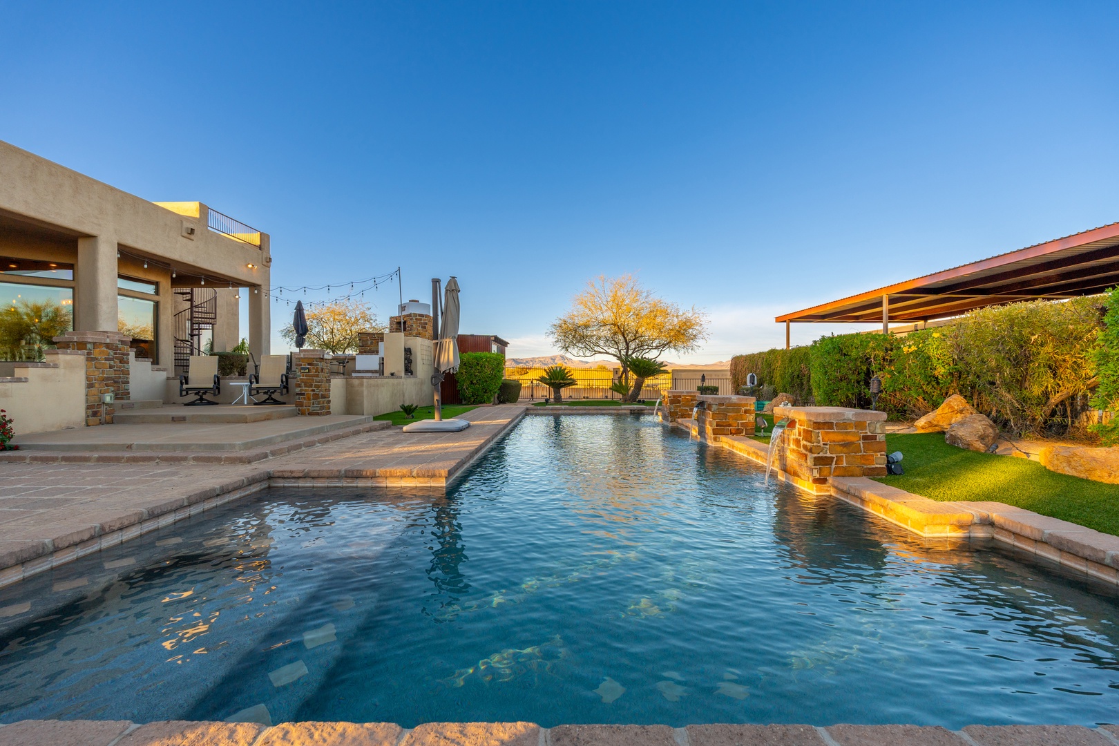 Your private oasis awaits with a stunning pool surrounded by desert landscaping, covered patios, and breathtaking views stretching to the horizon under endless blue skies.