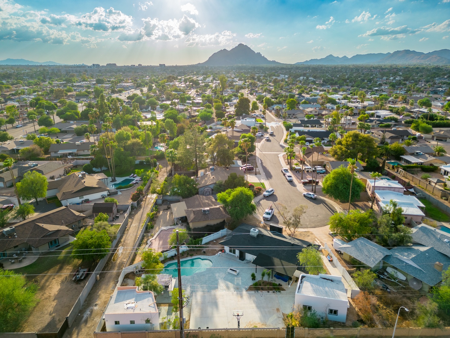 Aerial view of the property nestled in a peaceful residential neighborhood, with majestic mountain peaks visible in the distance and tree-lined streets creating a welcoming desert oasis.