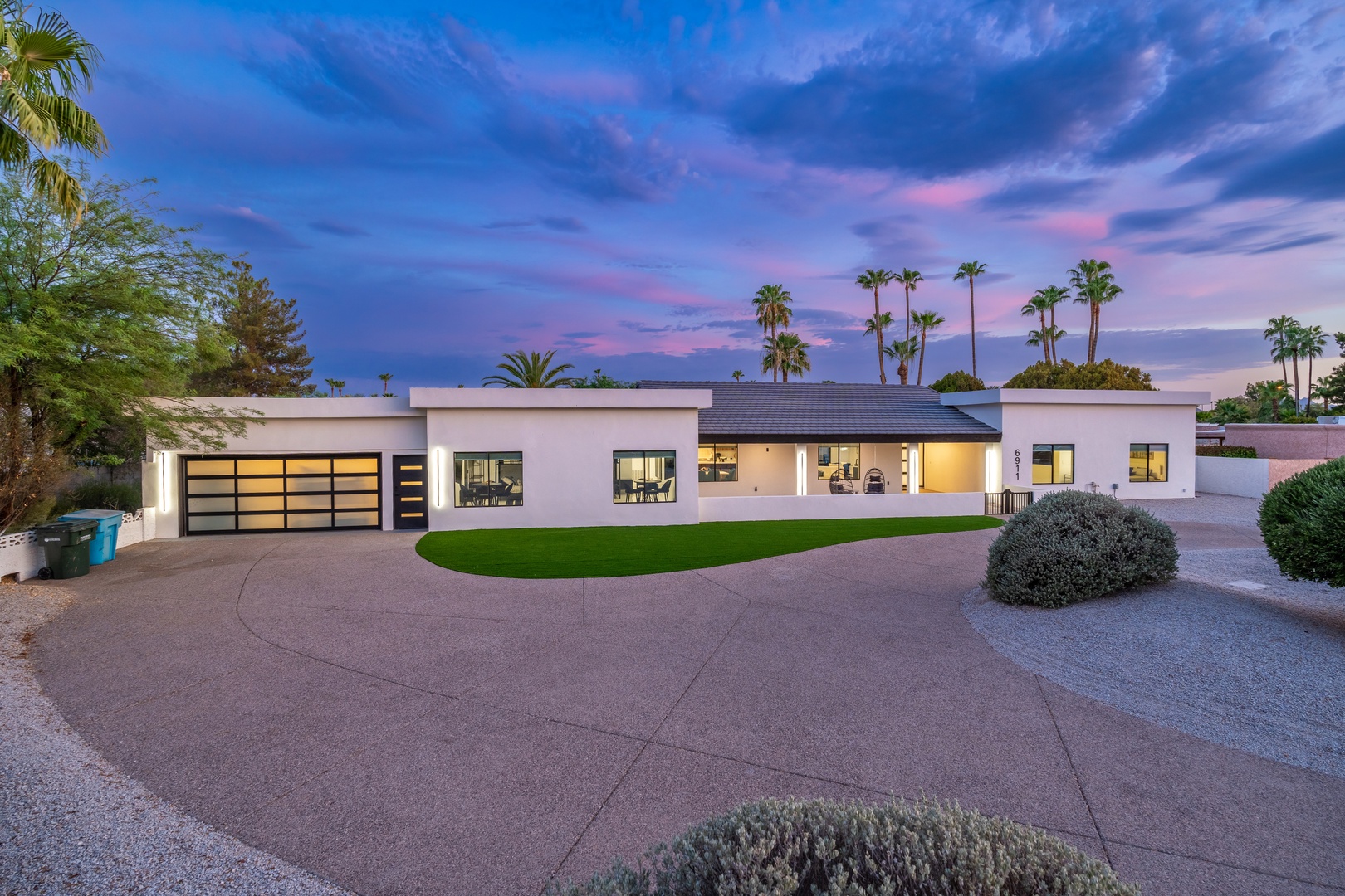 Modern desert retreat with sleek architecture and lush palm trees framing the property as evening twilight colors the sky.