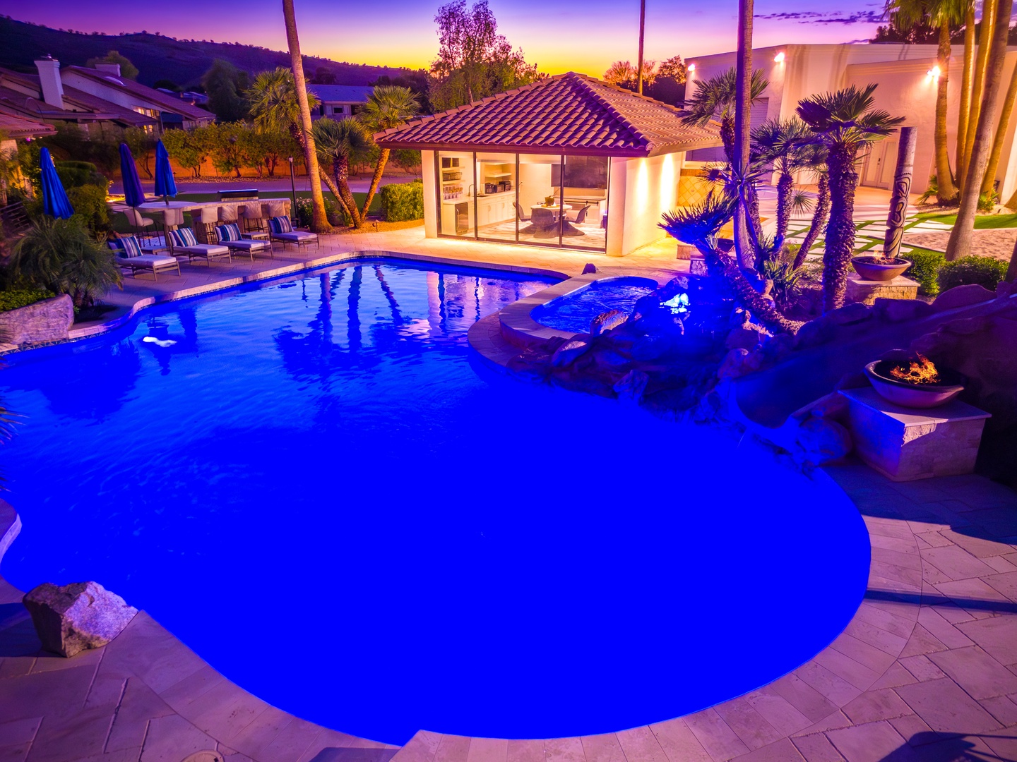 A stunning sunset casts vibrant hues over the resort-style pool and tropical gardens, creating an enchanting evening atmosphere at this luxurious vacation retreat.