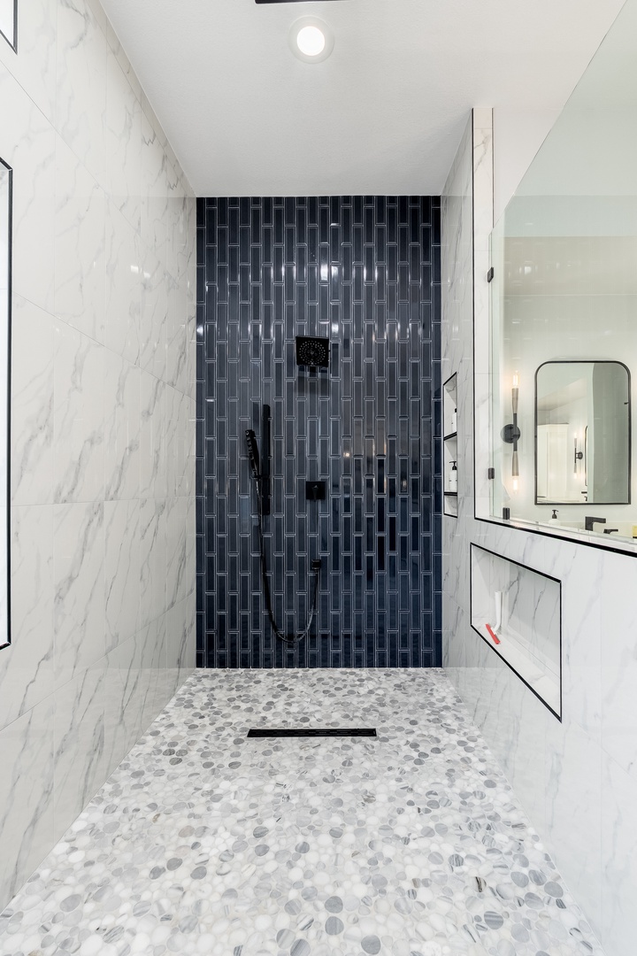 Step into your private spa-like shower featuring stunning marble walls and a sleek navy accent wall, with a rainfall showerhead and smooth pebble flooring under your feet.
