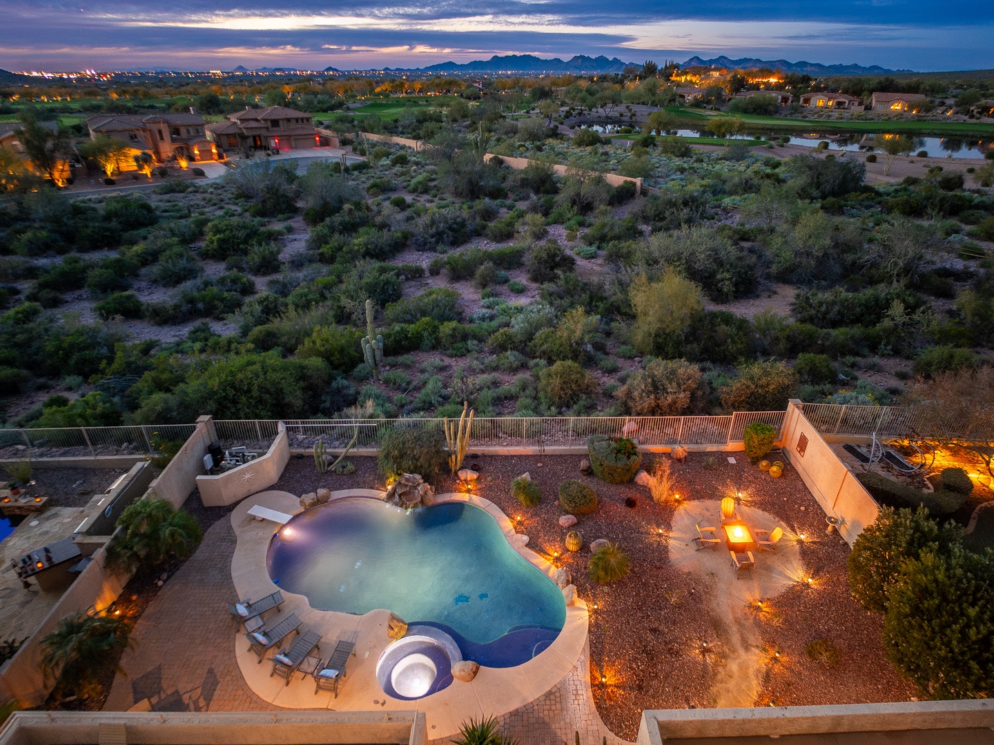 Aerial view of the property showcasing a private pool, spa, and expansive desert landscaping at twilight, surrounded by natural terrain and neighboring homes.