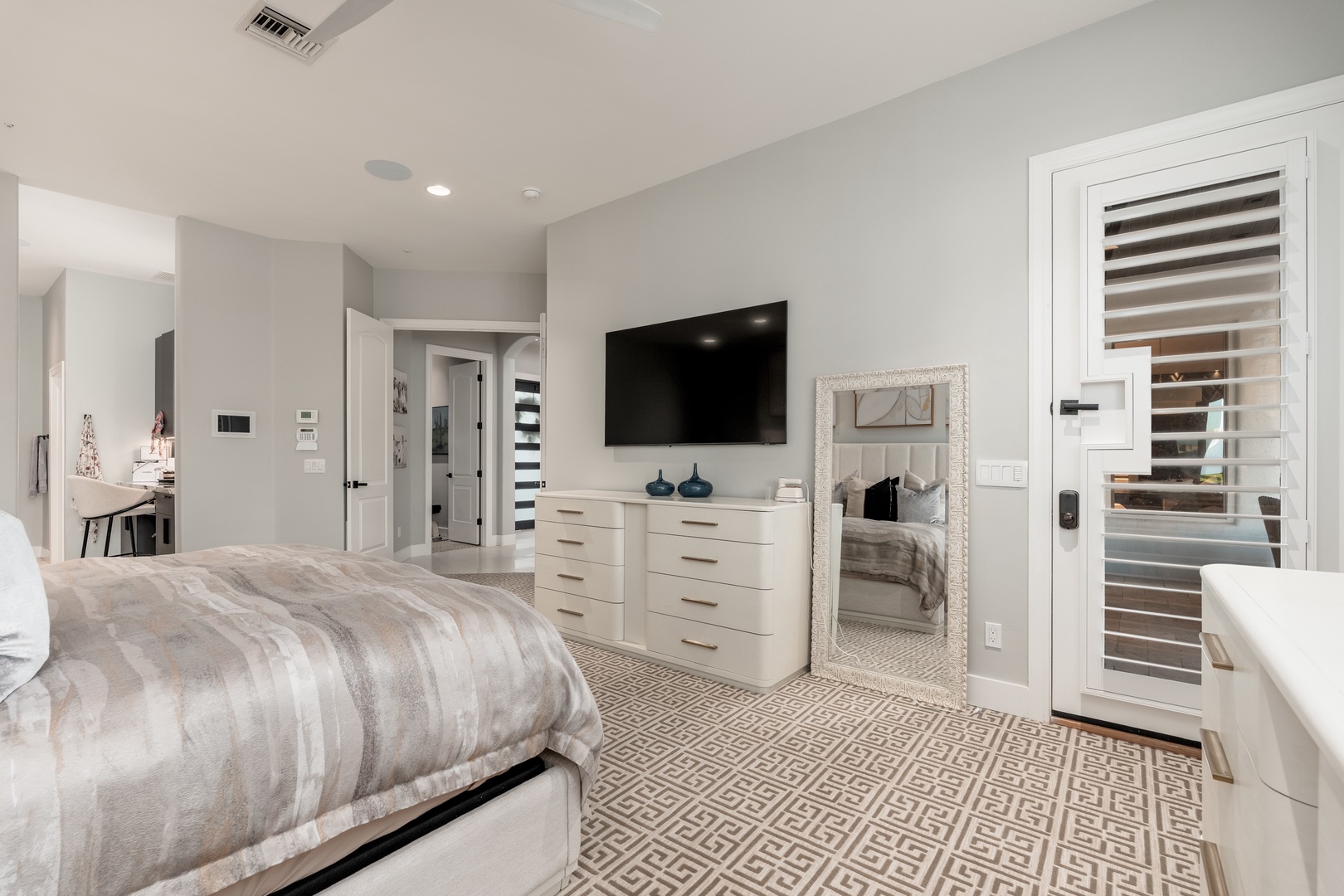 Your spacious suite blends comfort and style with a plush bed, sleek TV setup, and elegant mirror. Enjoy modern convenience with climate control and a private ensuite visible beyond.