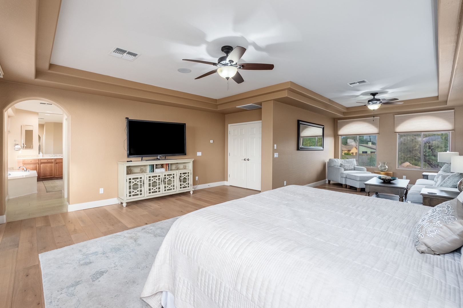 Your spacious master suite offers a cozy retreat with tray ceilings, a plush bed, separate sitting area, and bright windows overlooking serene views.