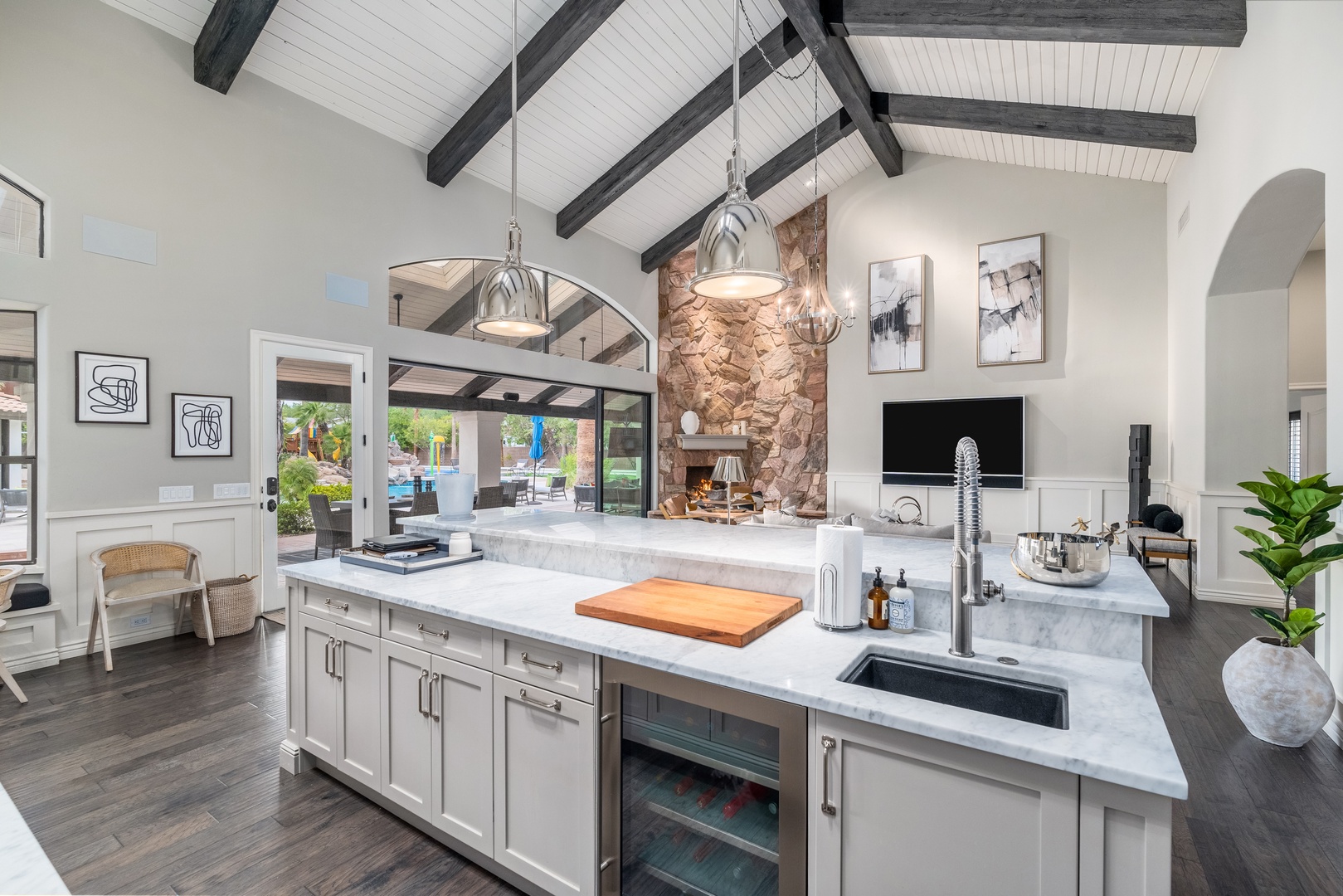 Your gourmet kitchen opens to a sparkling pool, blending sleek marble counters, rustic stone fireplace, and soaring beamed ceilings into one stunning, light-filled retreat.