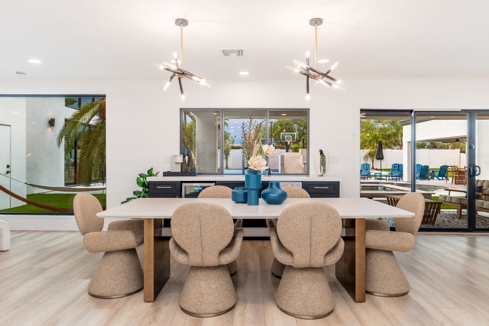 Picture yourself gathering around this elegant dining table with friends and family, basking in natural light from floor-to-ceiling windows overlooking lush tropical palms and inviting outdoor spaces.