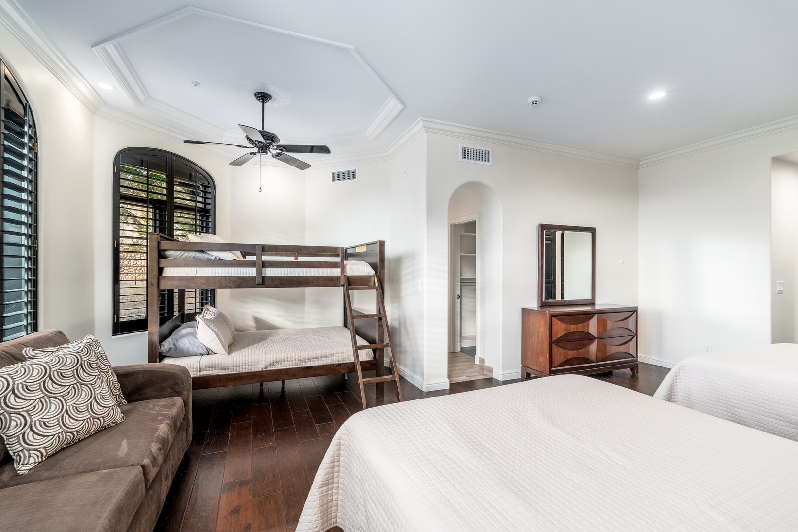 Your spacious bedroom features rich hardwood floors, elegant crown molding, and both a bunk bed and queen bed—perfect for families. Relax on the cozy sofa or enjoy the ceiling fan's gentle breeze.