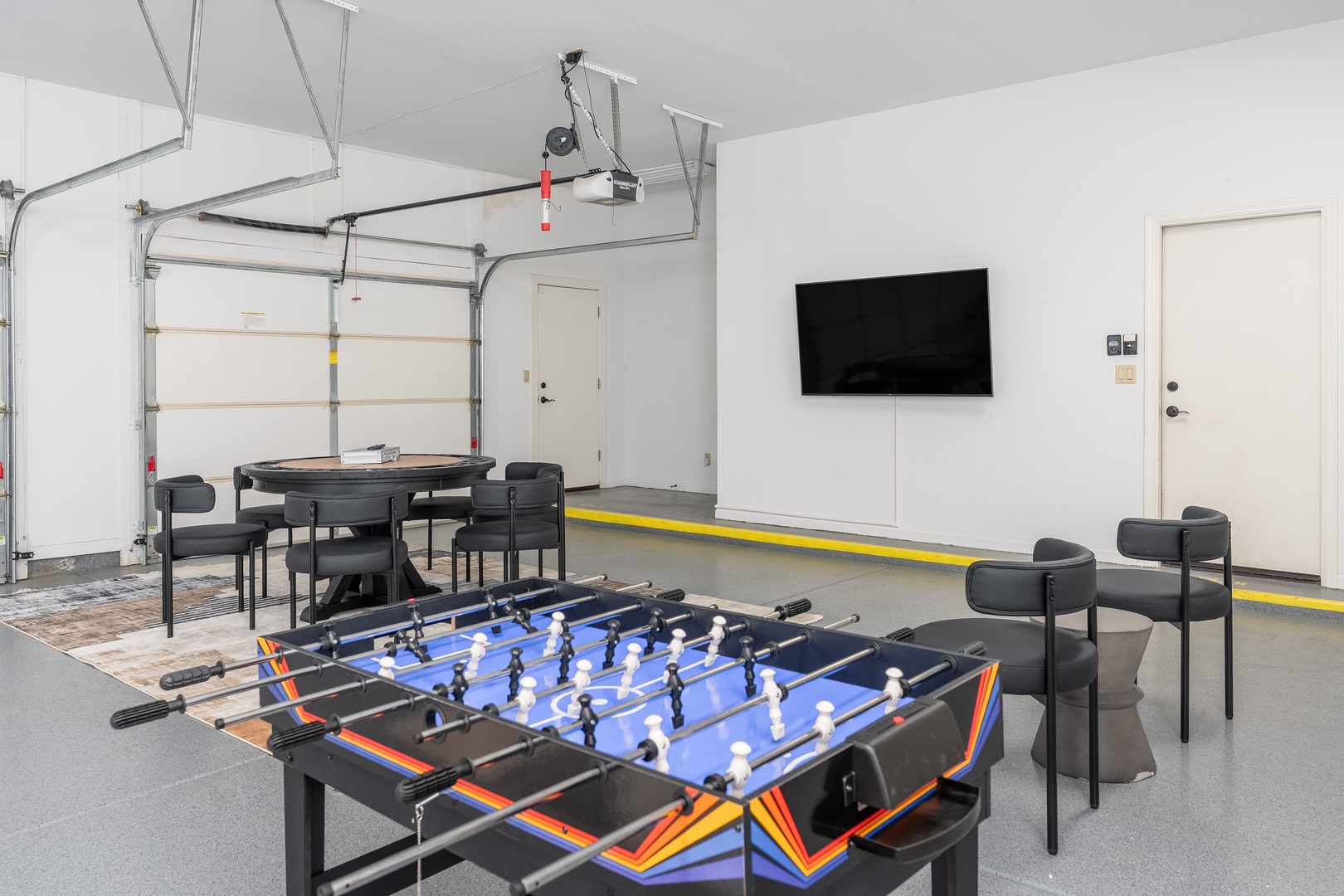 A converted garage game room featuring a foosball table, card table, and wall-mounted TV creates your perfect space for friendly competition and downtime with your group.