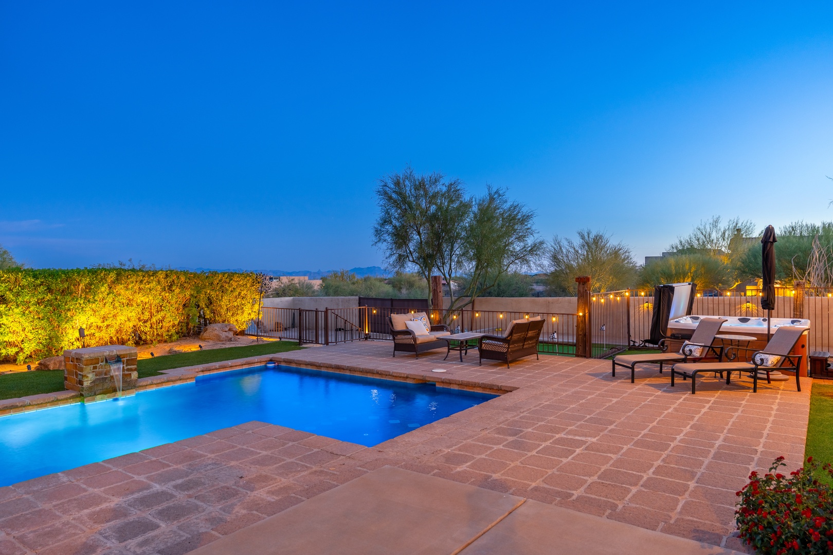 A stunning twilight view of the property's pool area, perfectly designed for relaxation and entertaining, set against the beauty of surrounding desert mountains and golden-lit trees.