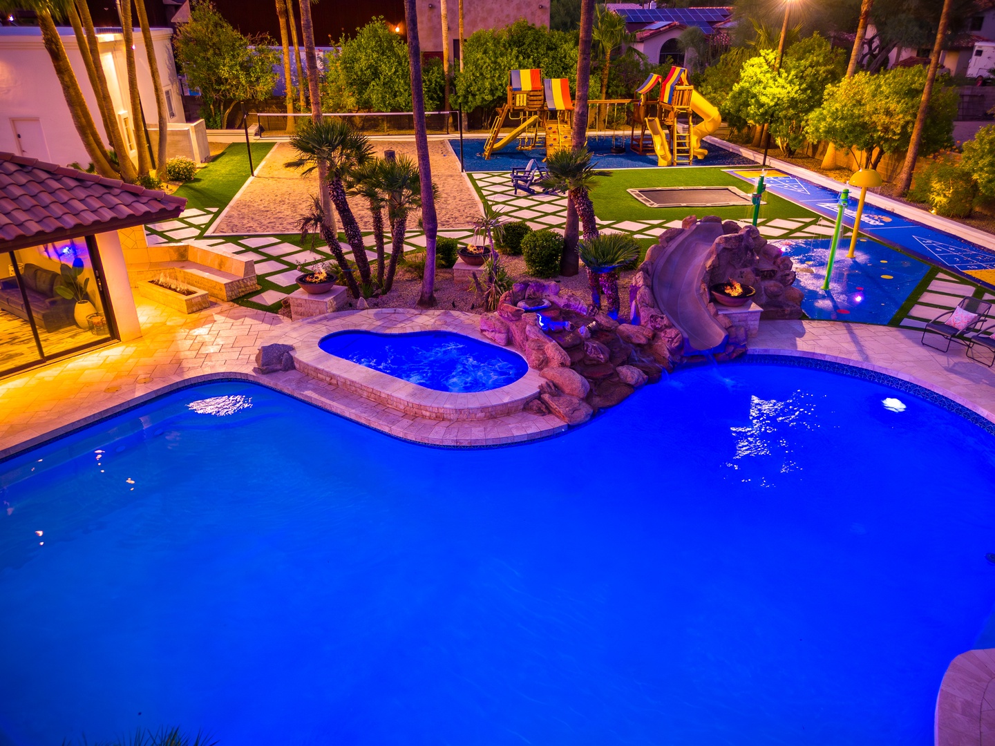 This aerial view showcases an expansive resort-style backyard featuring multiple pools, waterslides, children's playground, and lush tropical landscaping—perfect for families seeking a private retreat.