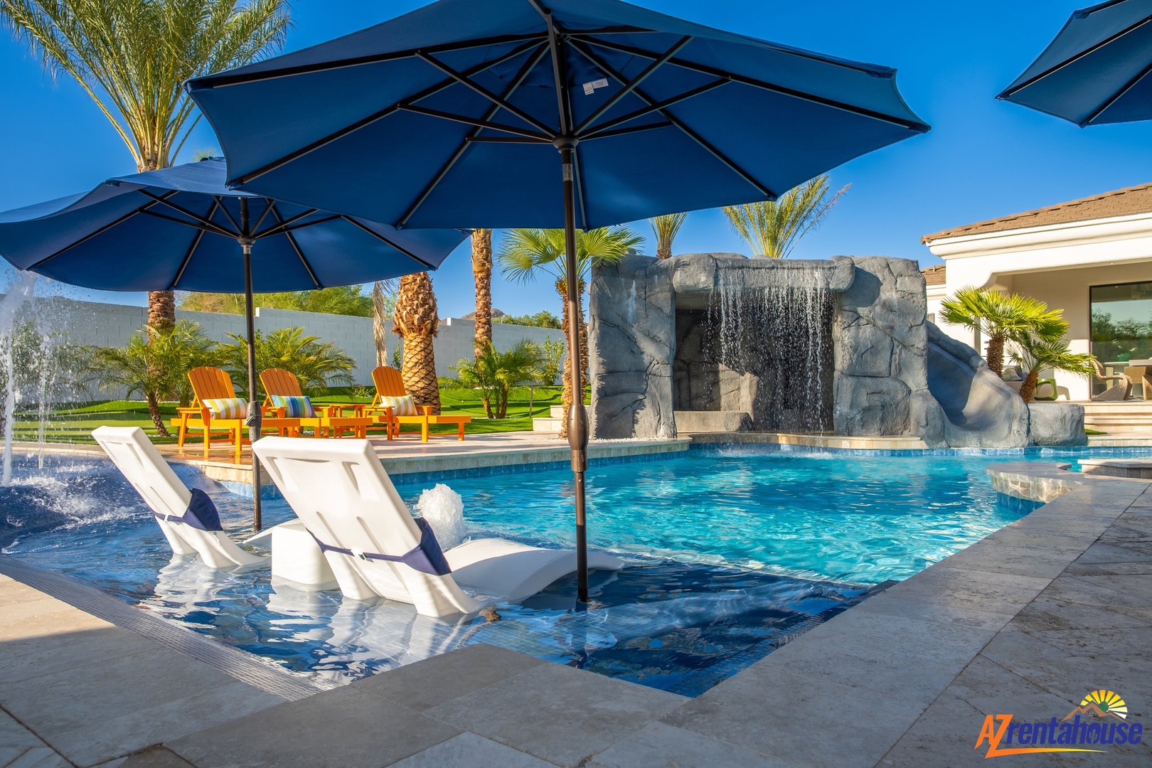 Luxurious pool oasis featuring dramatic waterfall, in-water loungers, and tropical palms under bright desert skies.