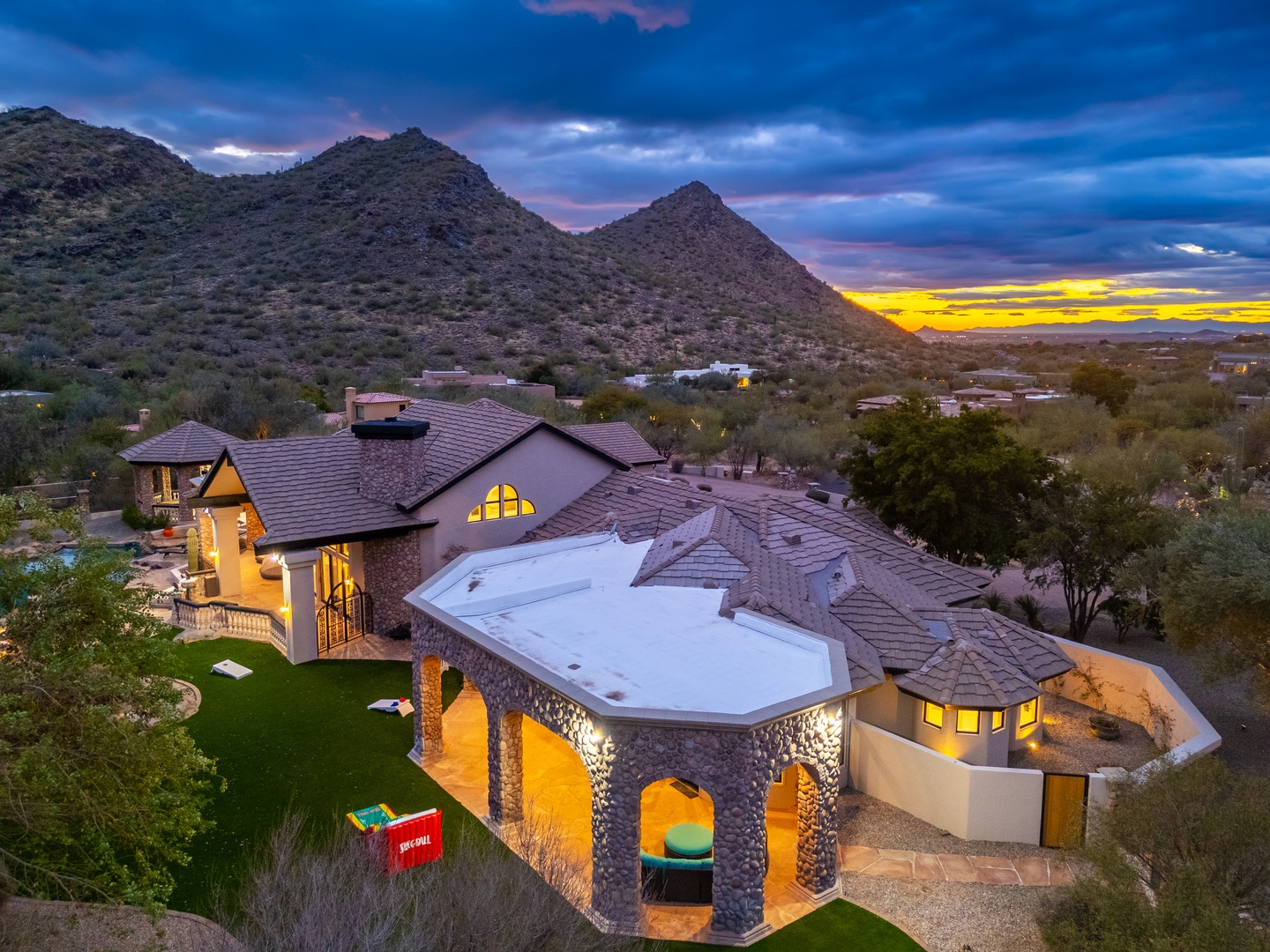 A stunning desert estate nestled against dramatic mountain peaks, captured at golden hour as the sun sets over the surrounding landscape.