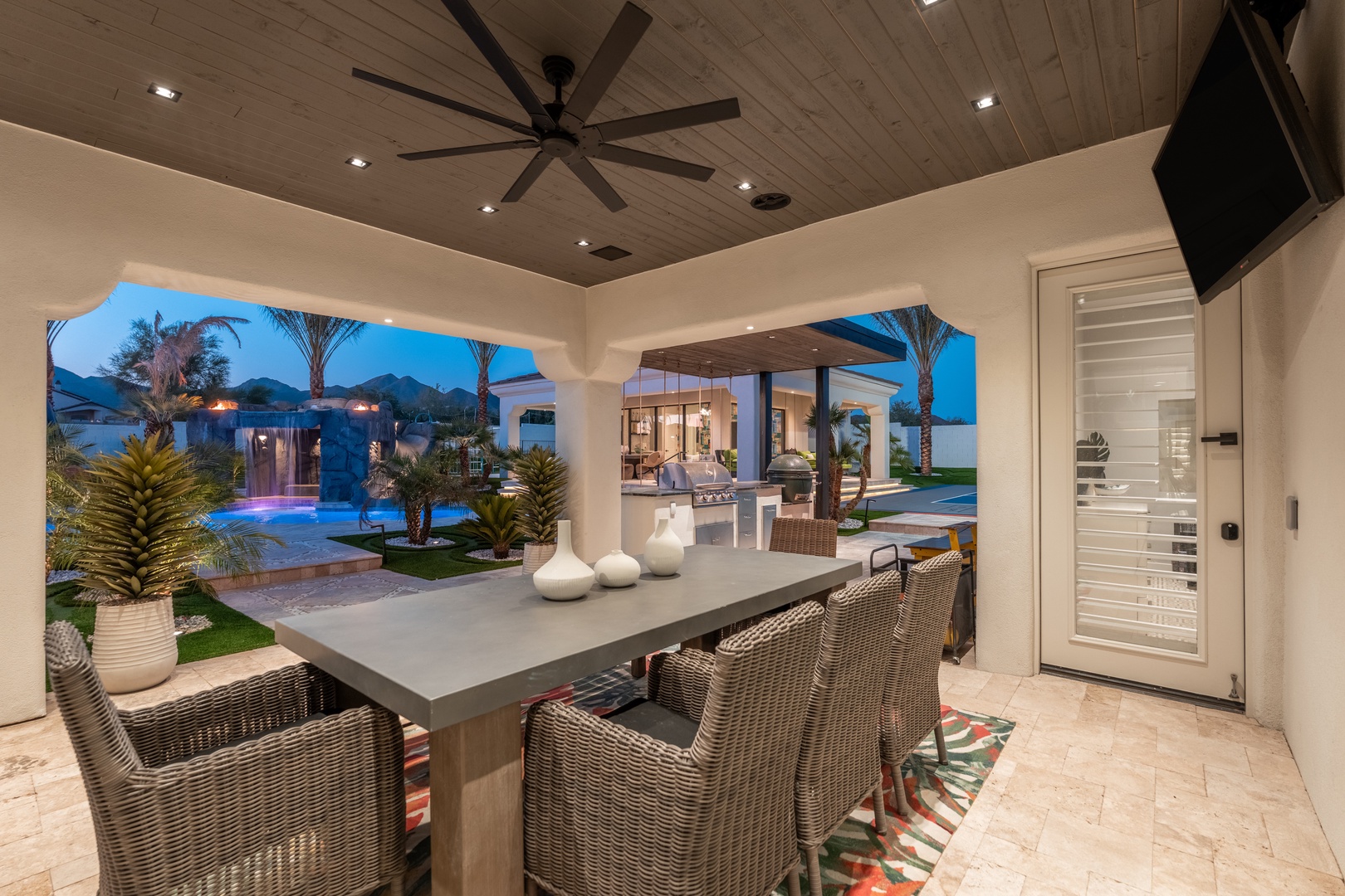 This covered patio blends indoor luxury with outdoor living, with a ceiling fan keeping you comfortable as you dine overlooking the sparkling pool, lush landscaping, and desert mountain views.